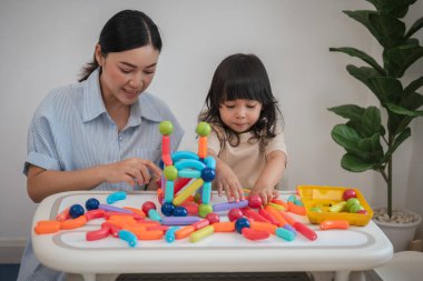 Küçük kız ve annesi evde renkli manyetik inşaat oyuncağı oynuyorlar.