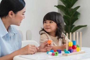 Küçük kız ve annesi evde eğitici tahta oyuncaklarla oynuyorlar.
