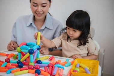 Küçük kız ve annesi evde renkli manyetik inşaat oyuncağı oynuyorlar.
