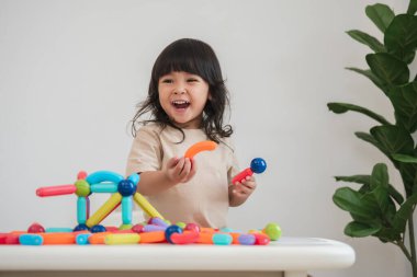 Küçük kız evde renkli manyetik inşaat oyuncağı oynuyor.