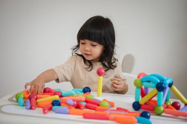 Küçük kız evde renkli manyetik inşaat oyuncağı oynuyor.