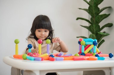 Küçük kız evde renkli manyetik inşaat oyuncağı oynuyor.