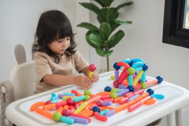 Küçük kız evde renkli manyetik inşaat oyuncağı oynuyor.