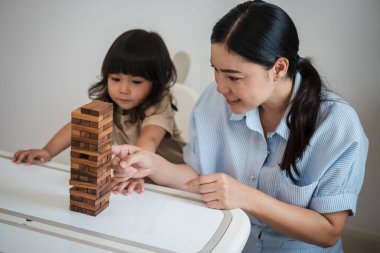 Küçük kız annesiyle birlikte tahta blok oyuncağı oynuyor.