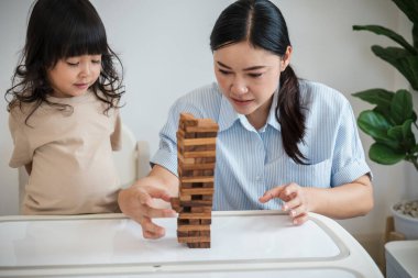 Küçük kız annesiyle birlikte tahta blok oyuncağı oynuyor.