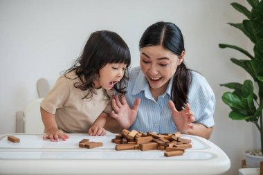 Küçük kız annesiyle birlikte tahta blok oyuncağı oynuyor ve kule çökmesiyle şok oluyor.