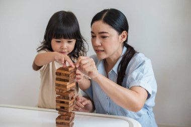 Küçük kız annesiyle birlikte tahta blok oyuncağı oynuyor.
