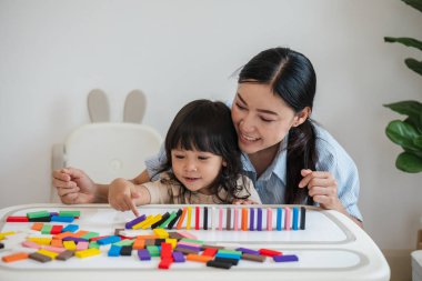 Küçük kız ve annesi renkli tahta blok oyuncakları ya da domino oyunu oynuyorlar.