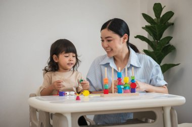 Küçük kız ve annesi evde eğitici tahta oyuncaklarla oynuyorlar.