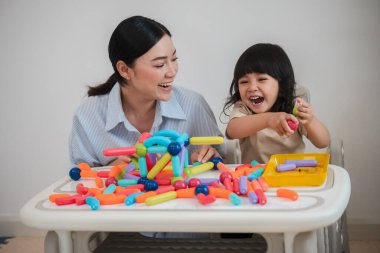 Küçük kız ve annesi evde renkli manyetik inşaat oyuncağı oynuyorlar.