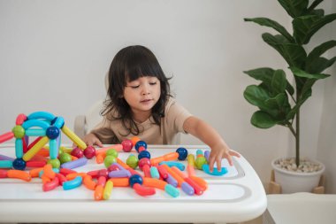 Küçük kız evde renkli manyetik inşaat oyuncağı oynuyor.