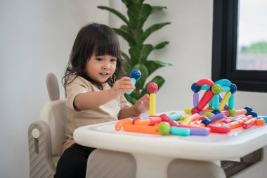 Küçük kız evde renkli manyetik inşaat oyuncağı oynuyor.