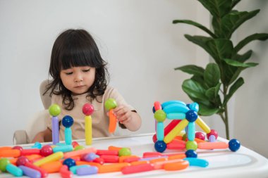 Küçük kız evde renkli manyetik inşaat oyuncağı oynuyor.