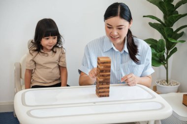 Küçük kız annesiyle birlikte tahta blok oyuncağı oynuyor.