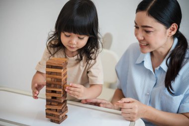 Küçük kız annesiyle birlikte tahta blok oyuncağı oynuyor.