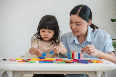 Küçük kız ve annesi renkli tahta blok oyuncakları ya da domino oyunu oynuyorlar.