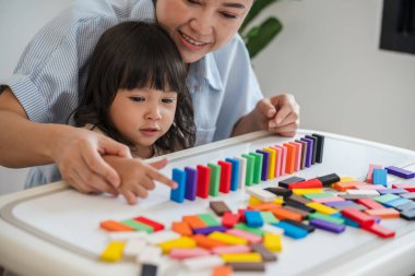 Küçük kız ve annesi renkli tahta blok oyuncakları ya da domino oyunu oynuyorlar.