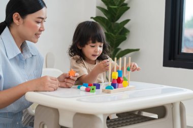 Küçük kız ve annesi evde eğitici tahta oyuncaklarla oynuyorlar.