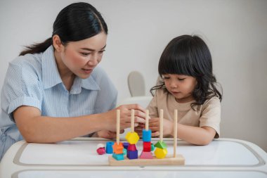 Küçük kız ve annesi evde eğitici tahta oyuncaklarla oynuyorlar.