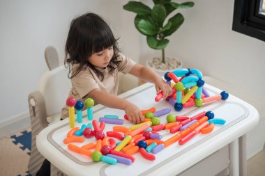 Küçük kız evde renkli manyetik inşaat oyuncağı oynuyor.