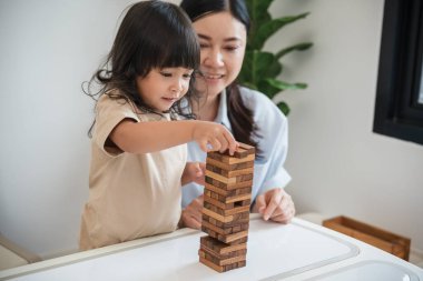 Küçük kız annesiyle birlikte tahta blok oyuncağı oynuyor.