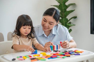 Küçük kız ve annesi renkli tahta blok oyuncakları ya da domino oyunu oynuyorlar.