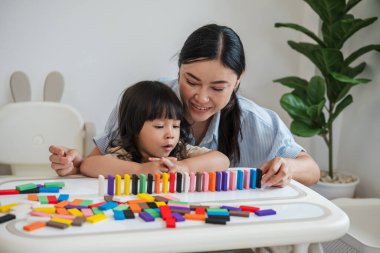 Küçük kız ve annesi renkli tahta blok oyuncakları ya da domino oyunu oynuyorlar.
