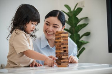 Küçük kız annesiyle birlikte tahta blok oyuncağı oynuyor.