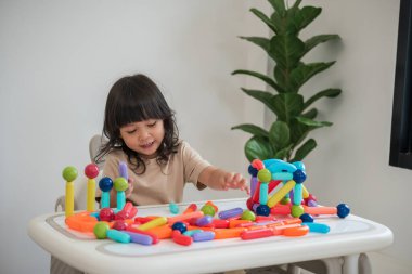 Küçük kız evde renkli manyetik inşaat oyuncağı oynuyor.