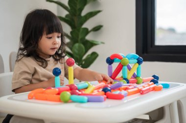 Küçük kız evde renkli manyetik inşaat oyuncağı oynuyor.