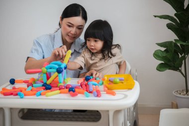 Küçük kız ve annesi evde renkli manyetik inşaat oyuncağı oynuyorlar.