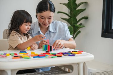 Küçük kız ve annesi renkli tahta blok oyuncakları ya da domino oyunu oynuyorlar.