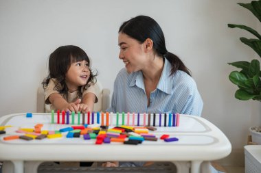Küçük kız ve annesi renkli tahta blok oyuncakları ya da domino oyunu oynuyorlar.