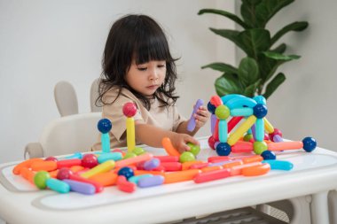 Küçük kız evde renkli manyetik inşaat oyuncağı oynuyor.