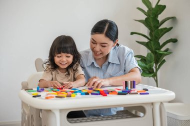 Küçük kız ve annesi renkli tahta blok oyuncakları ya da domino oyunu oynuyorlar.