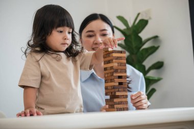Küçük kız annesiyle birlikte tahta blok oyuncağı oynuyor.