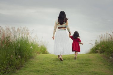 Anne küçük kızıyla çim tarlasında yürüyor.