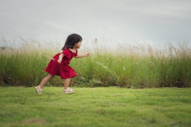 Kırmızı elbiseli mutlu kız çim tarlasında koşuyor.