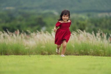 Kırmızı elbiseli mutlu kız çim tarlasında koşuyor.