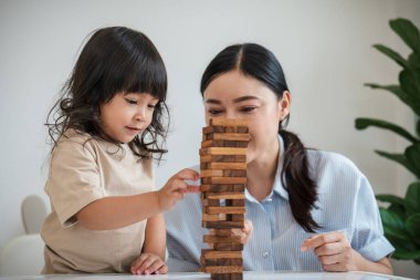 Küçük kız annesiyle birlikte tahta blok oyuncağı oynuyor.