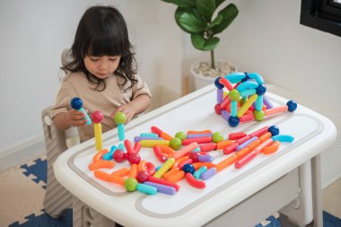 Küçük kız evde renkli manyetik inşaat oyuncağı oynuyor.