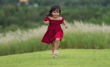 Kırmızı elbiseli mutlu kız çim tarlasında koşuyor.