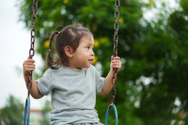 Neşeli küçük kız dışarıda salıncakta sallanıyor.