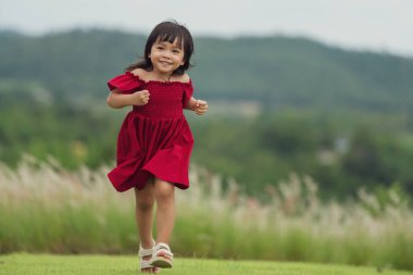 Kırmızı elbiseli mutlu kız çim tarlasında koşuyor.