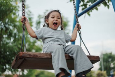 Neşeli küçük kız oyun parkında tahta salıncakta oynuyor.