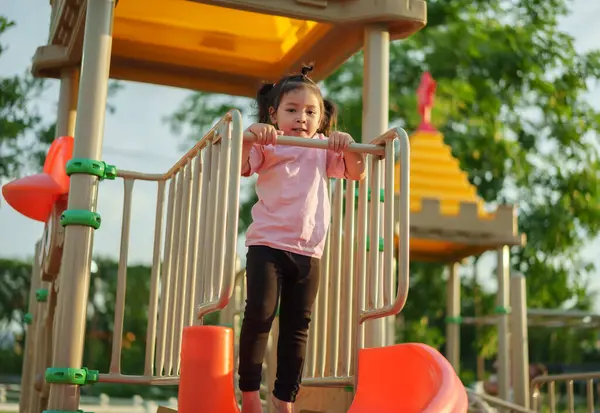 Parktaki çocuk parkında barın önünde elini sallayan küçük mutlu kız.