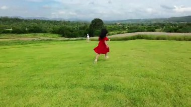 Kırmızı elbiseli mutlu kız çim tarlasında koşuyor.