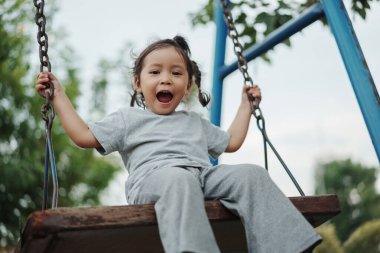 Neşeli küçük kız oyun parkında tahta salıncakta oynuyor.
