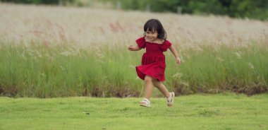 Kırmızı elbiseli mutlu kız çim tarlasında koşuyor.