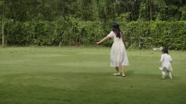 Anne ve küçük kız parkta çim tarlasında koşuşturmaca oynuyorlar.